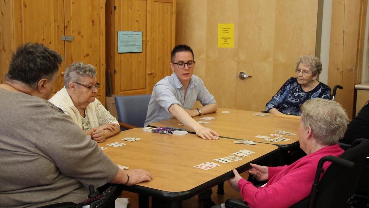 Un jeune homme joue aux cartes avec des personnes âgées.