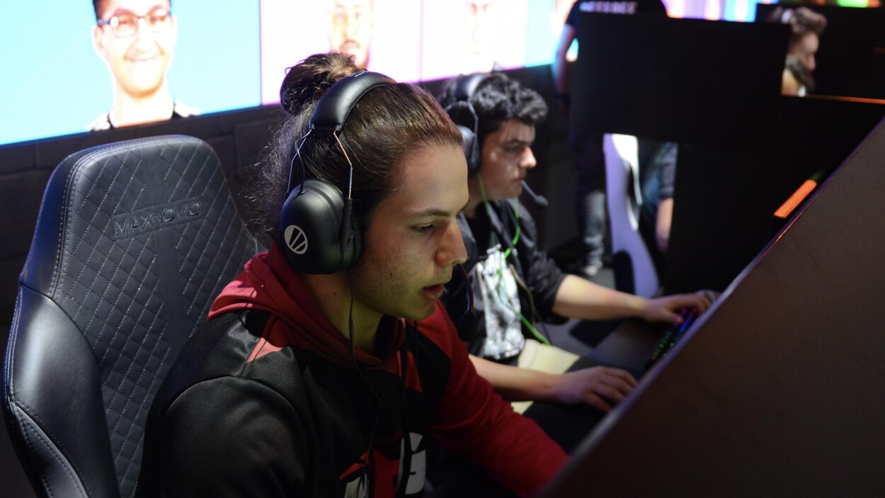 Deux jeunes hommes sont assis devant des écrans, portant des casques d'écoute, les mains sur le clavier alors qu'ils jouent à Fortnite.