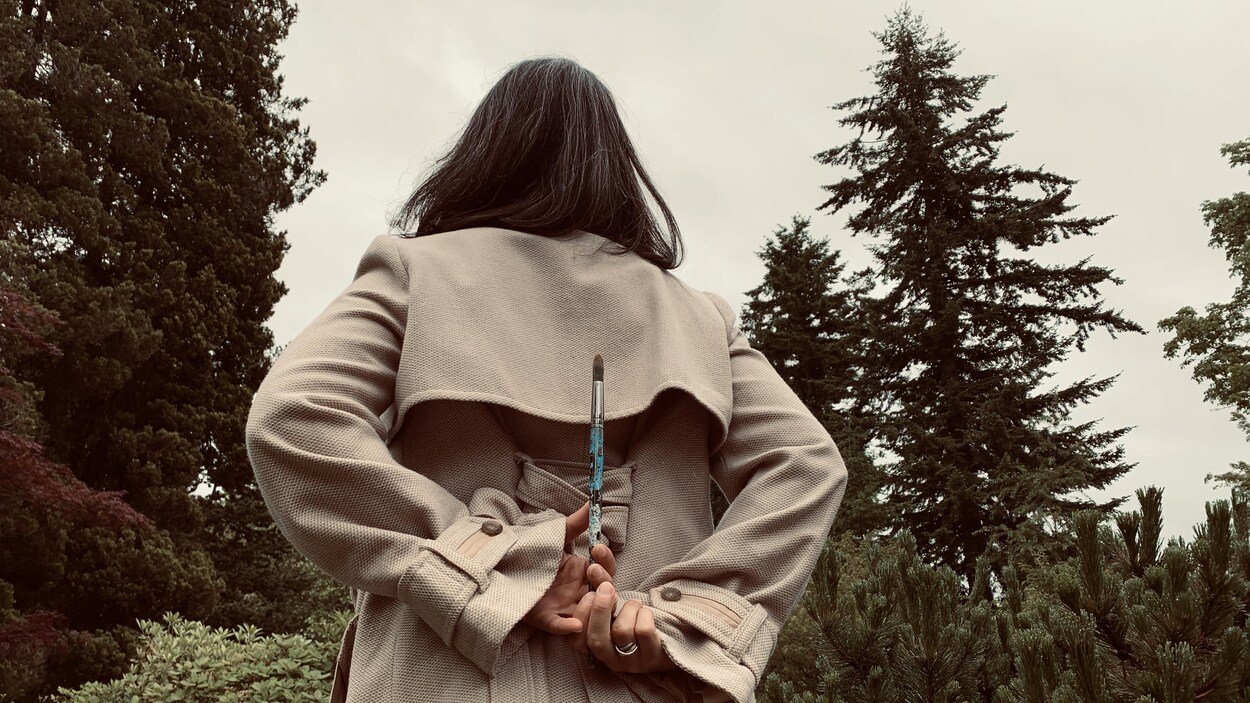 Femme de dos qui tient un pinceau entre ses mains.