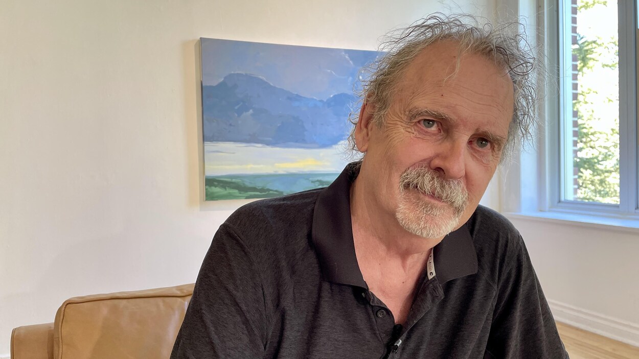 Homme assis devant une toile représentant un paysage.