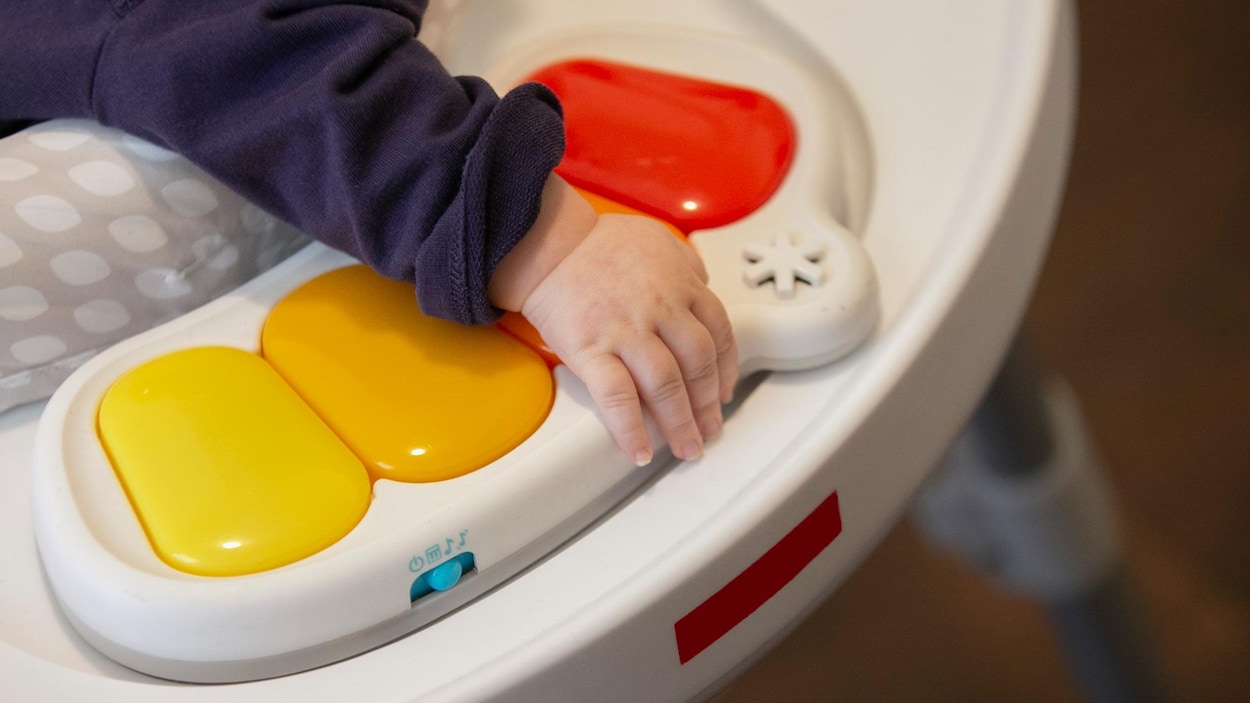 Un bébé dans une chaise sauteuse appuie sa main sur un jouet.