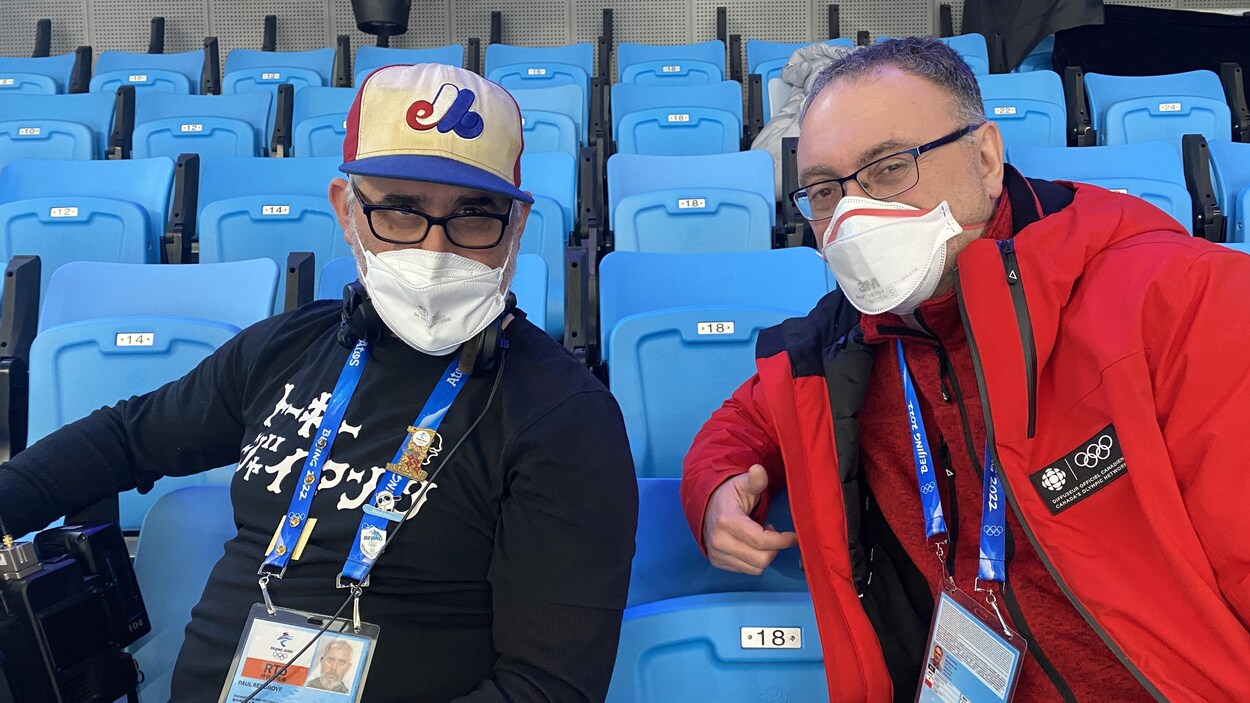 Un homme en noir avec une casquette de baseball assis à côté d'un homme en rouge