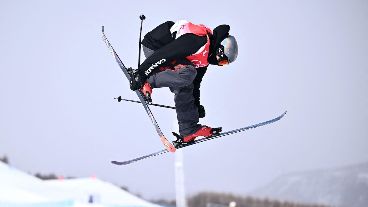 Un skieur canadien effectue une manœuvre en tenant son ski droit.