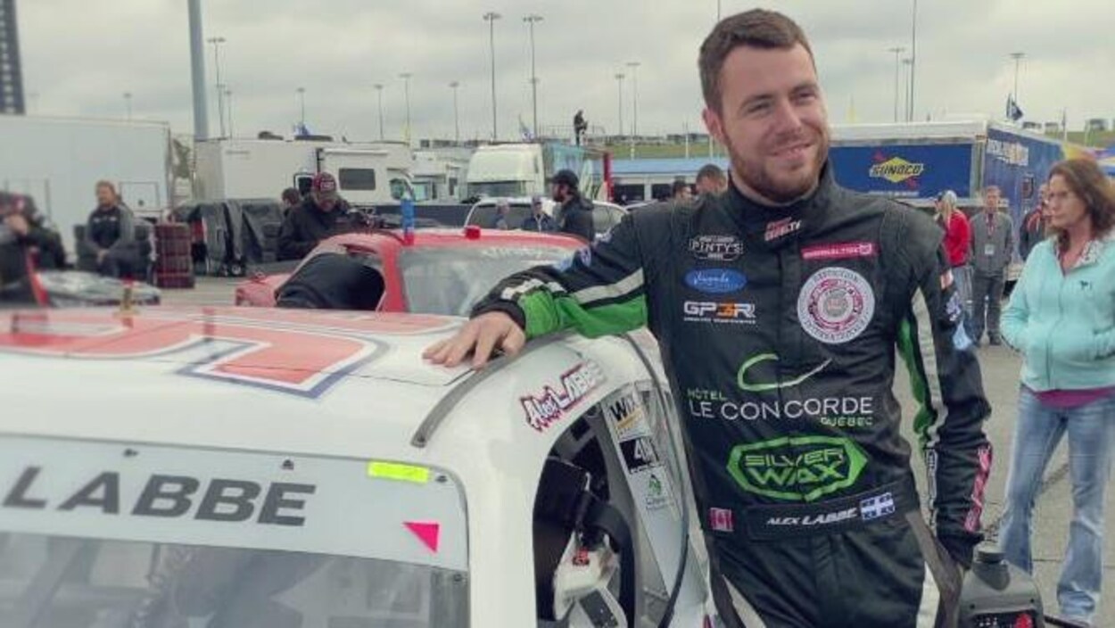Alex Labbé sourit, la main droite sur le toit de son auto