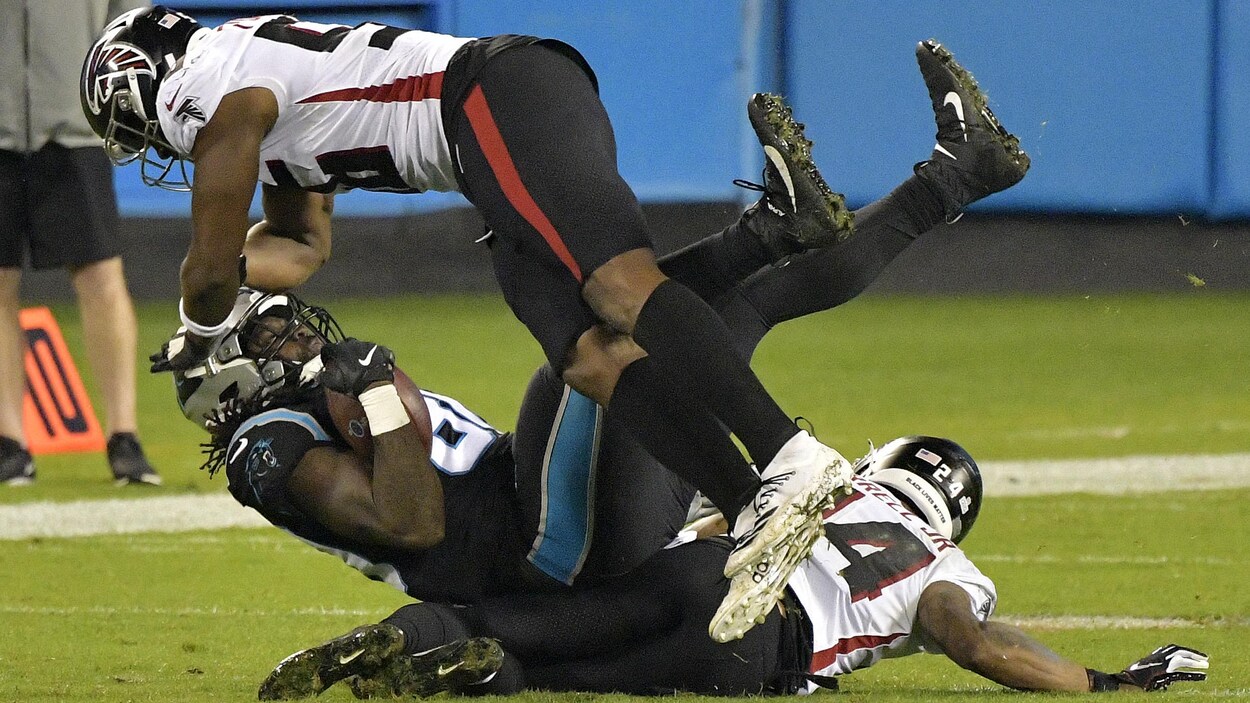 Deux joueurs de football plaquent un joueur adverse au sol.