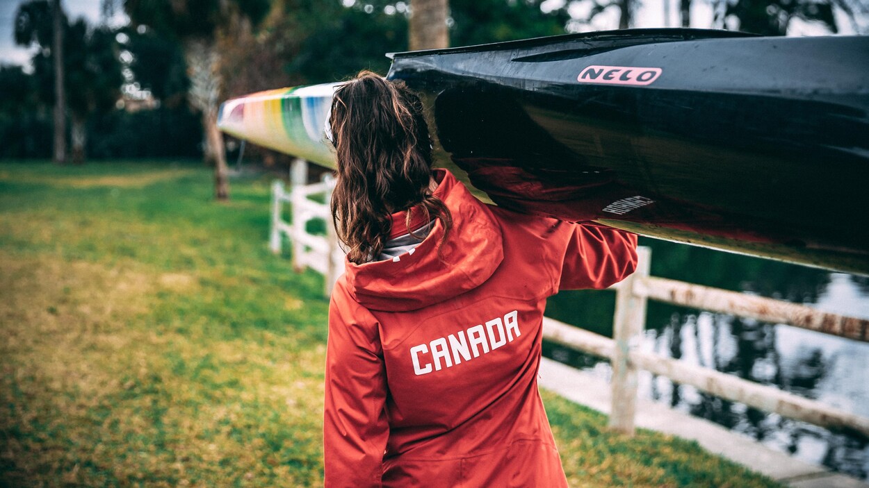Andréanne Langlois transporte son kayak sur une épaule. On la voit de dos. Andréanne Langlois transporte son kayak sur une épaule. On la voit de dos.