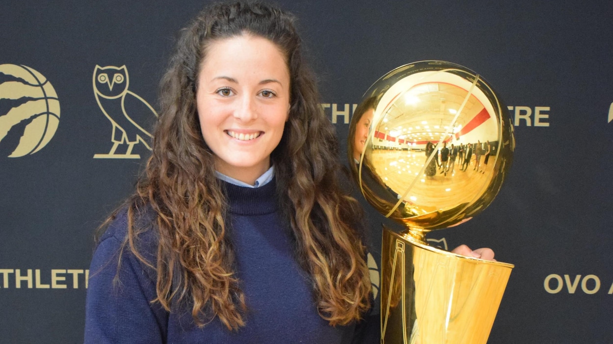 Une jeune entraîneuse de basketball tient le trophée de la NBA devant la caméra.