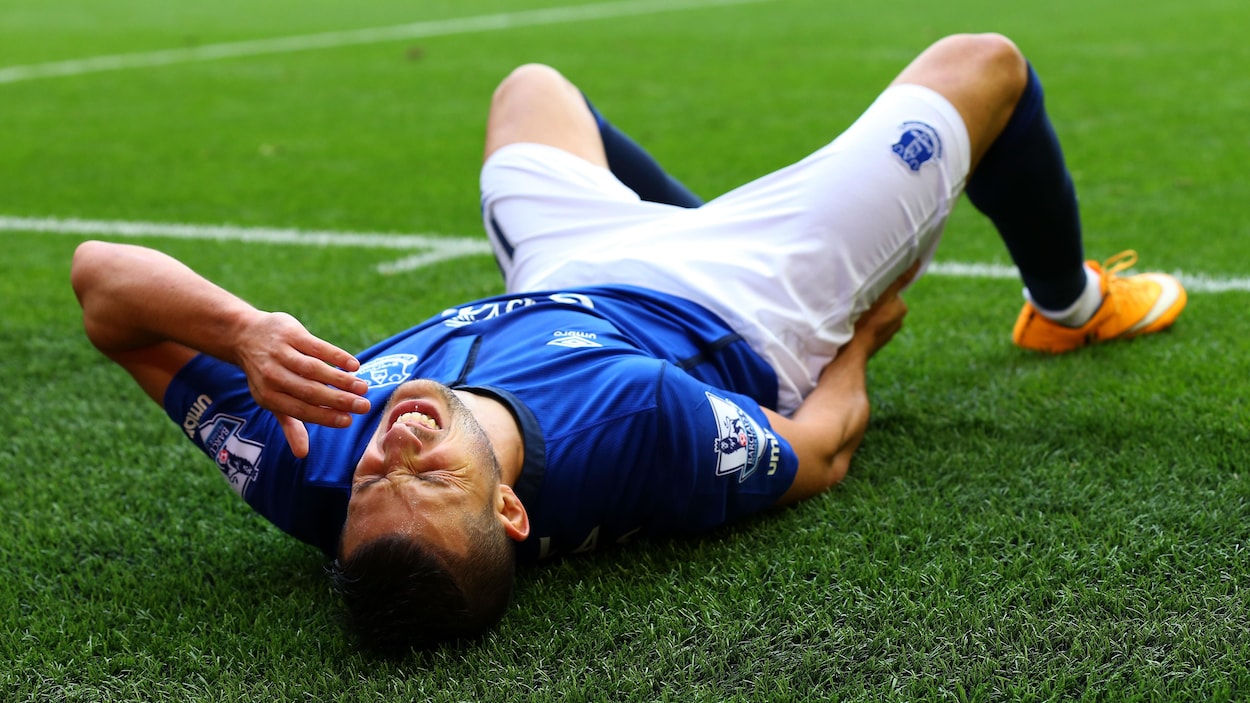 Un joueur de soccer dans un uniforme bleu se tord de douleur sur le terrain
