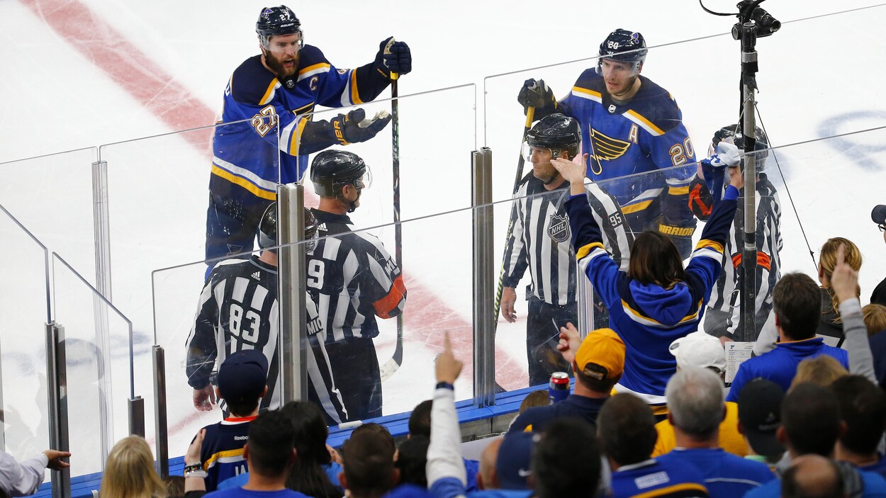 Trois arbitres sur la patinoire, entourés de deux joueurs mécontents.