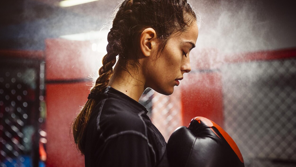 Une femme dans un gym avec des gants de boxe. Elle semble se concentrer.