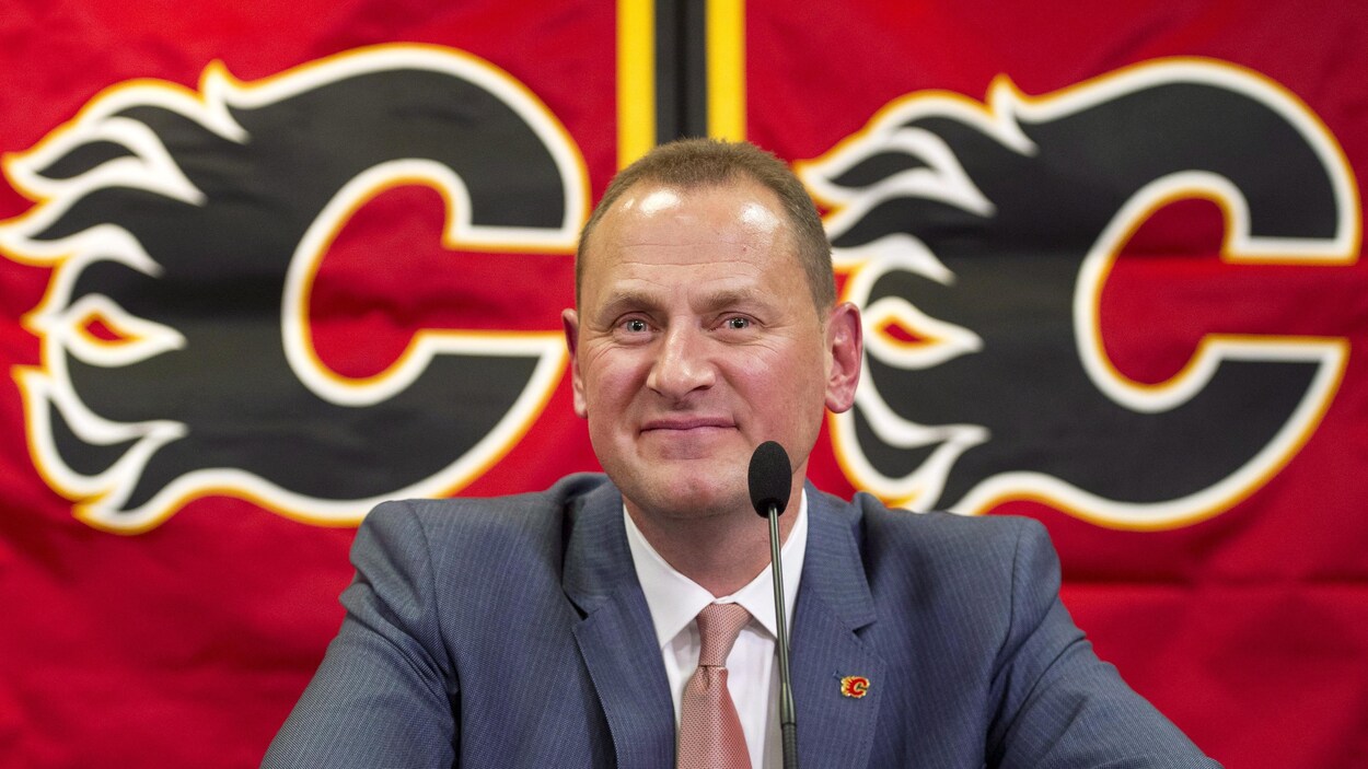 Il est en conférence de presse devant le logo des Flames.