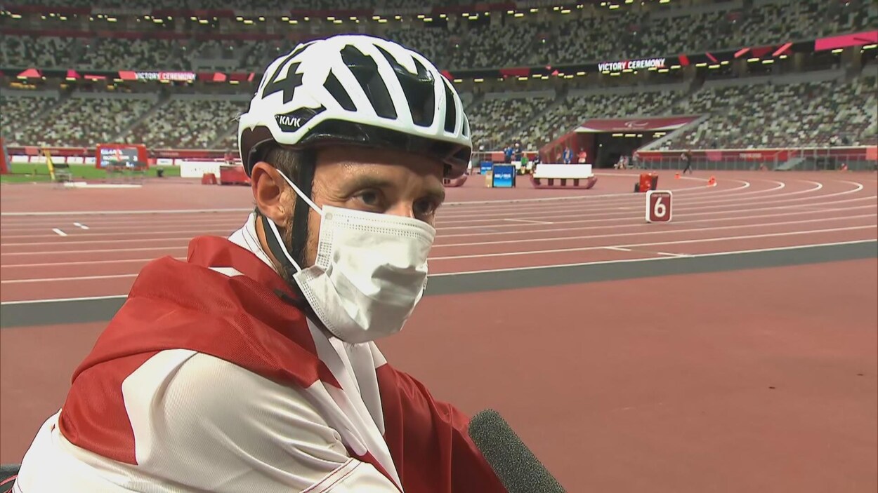 Le coureur en fauteuil roulant Brent Lakatos, avec son masque, répond aux questions d'un journaliste au Stade olympique de Tokyo.