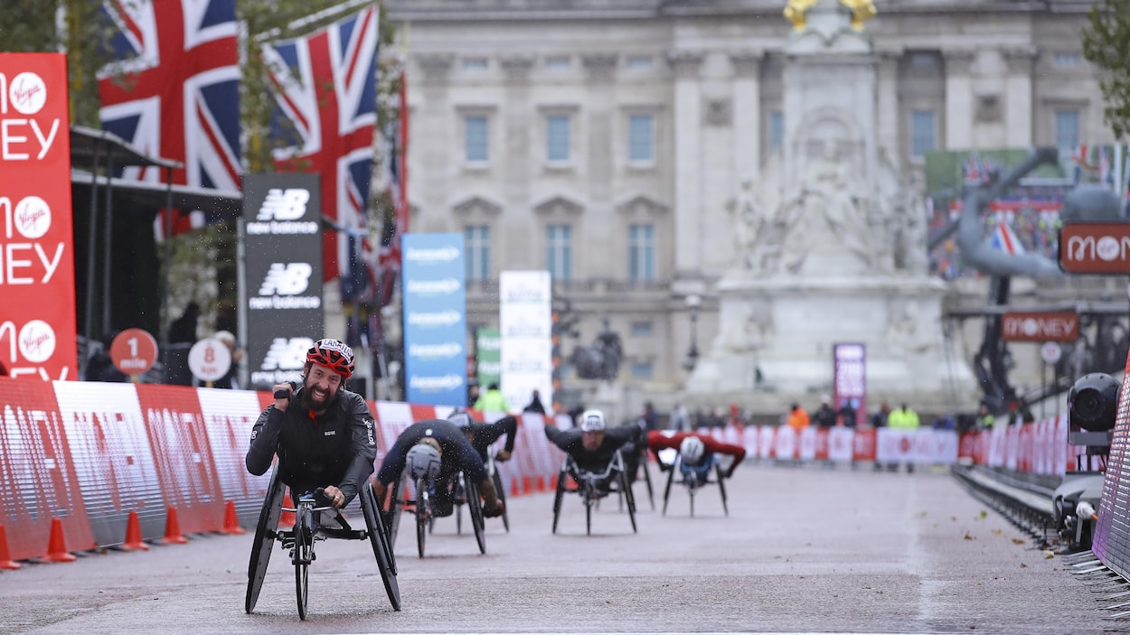 Un athlète en fauteuil roulant, vêtu de noir et d'un casque rouge, franchit le fil d'arrivée au marathon de Londres.