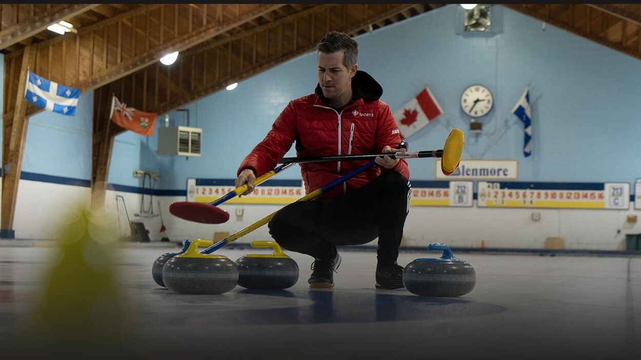 Un homme est accroupi sur la glace entouré de pierres de curling.