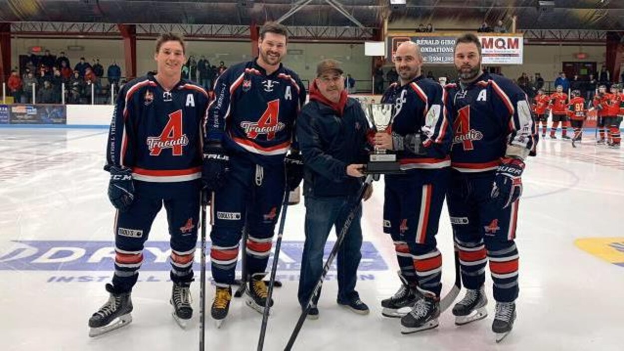 Joueurs de hockey côte-à-côtes, tenant un trophée.