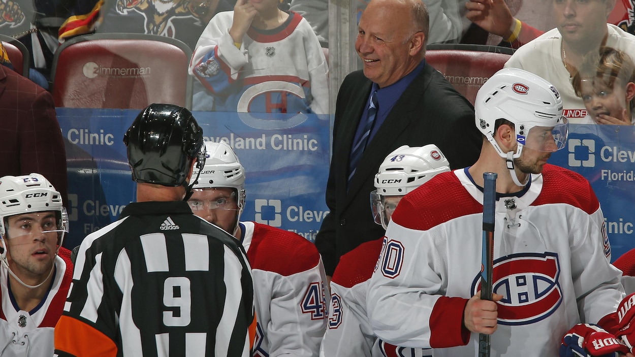 Un entraîneur de hockey derrière le banc de ses joueurs sourit à l'arbitre.