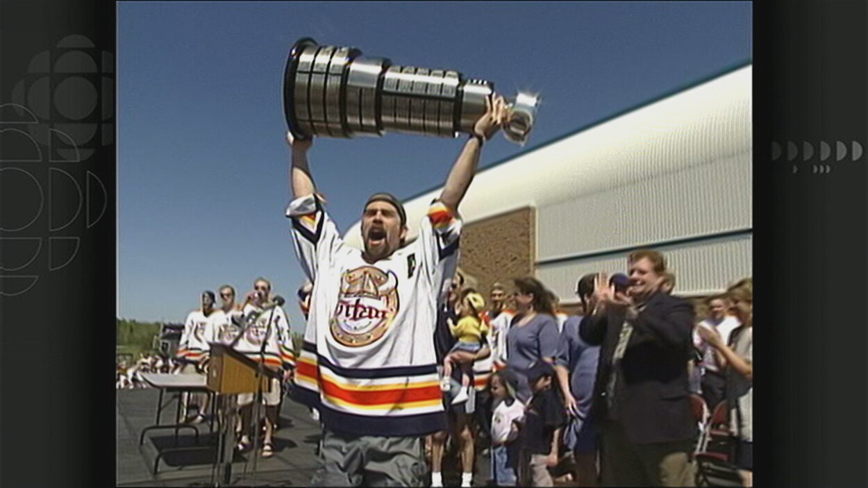 Un joueur lève le trophée en célébrant sur une estrade, devant le centre KC Irving. Un joueur lève le trophée en célébrant sur une estrade, devant le centre KC Irving.