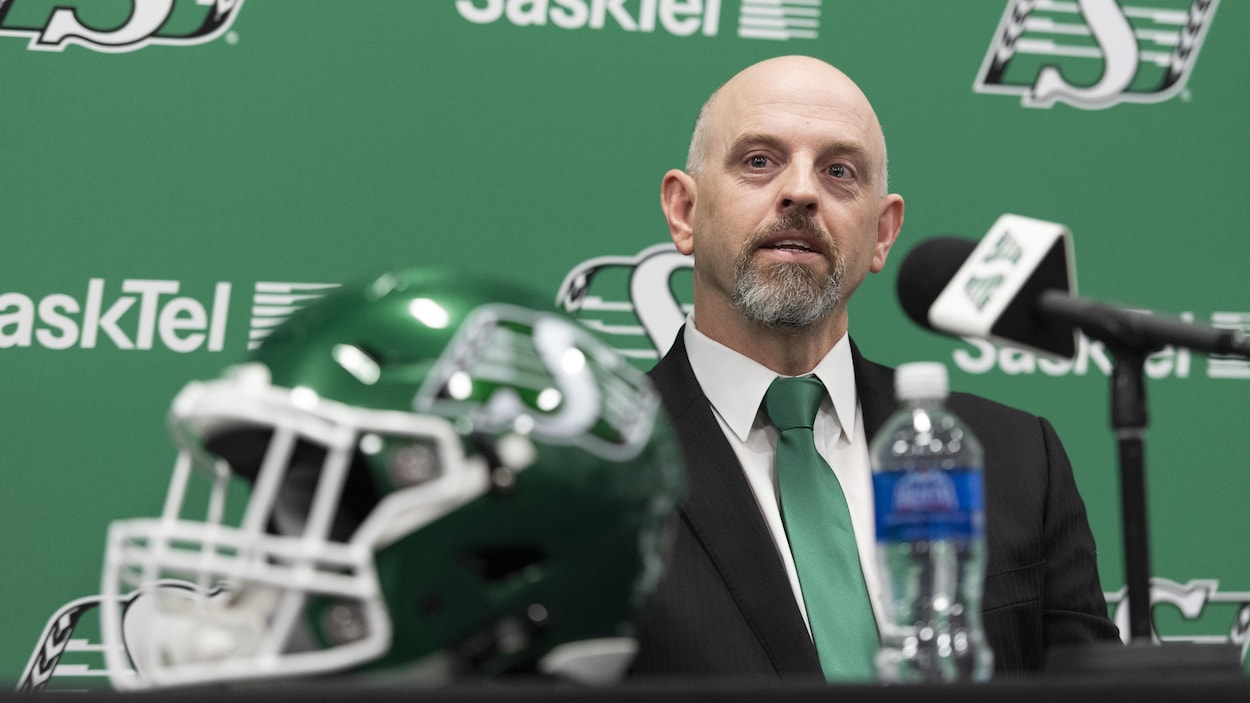 Craig Dickenson assis devant un micro. Il porte une cravate verte, la couleur officielle des Roughriders.