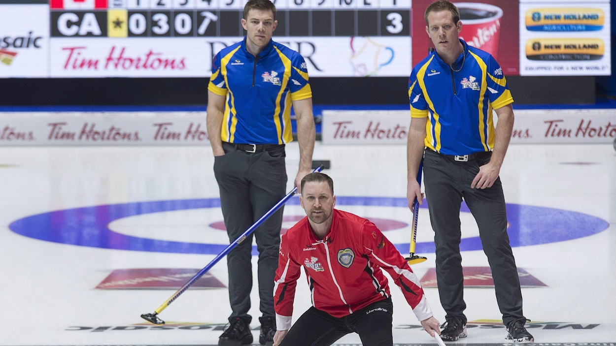 Le capitaine d'Équipe Canada, Brad Gushue, observe une pierre lancée par un coéquipier. Derrière lui, Brad Thiessen et Karrick Martin de l'Alberta observent aussi.