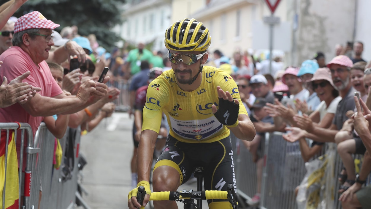 Un cycliste en jaune salue la foule qui l'acclame.