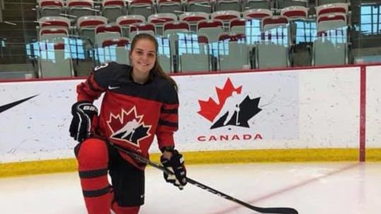 Dominique Cormier sourit et est agenouillée sur la patinoire avec son gilet et son équipement de hockey.