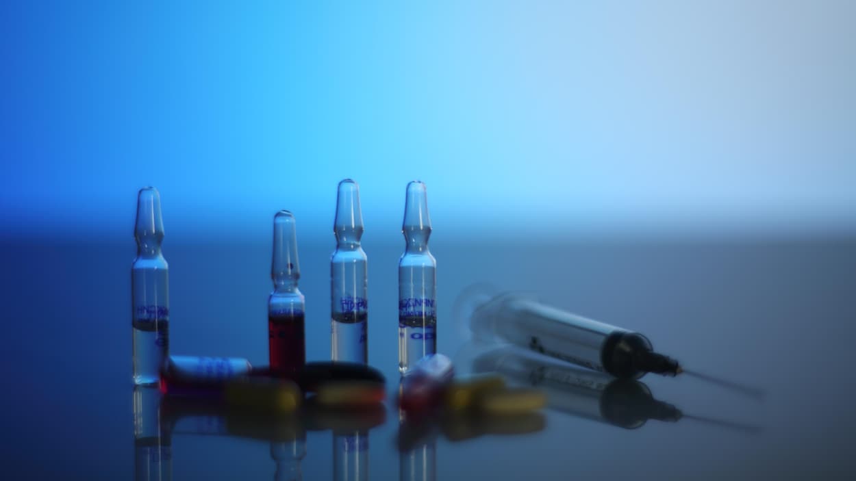Sur une table, quatre ampoules avec du liquide à l'intérieur, une seringue et des pilules.