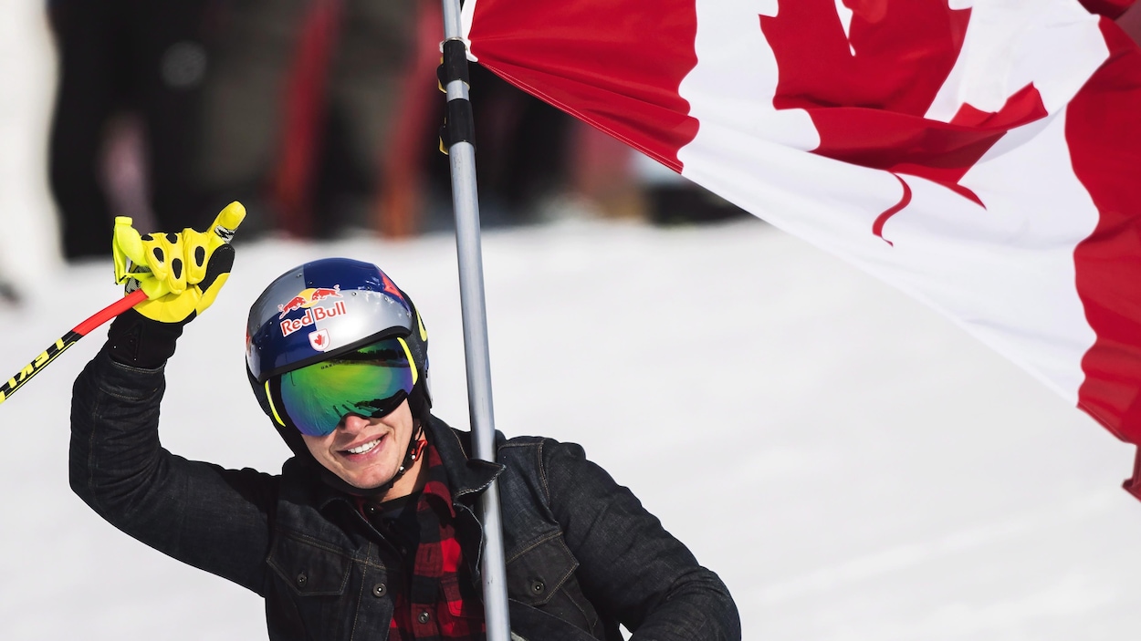Il lève un bras avec le drapeau canadien sur son épaule.