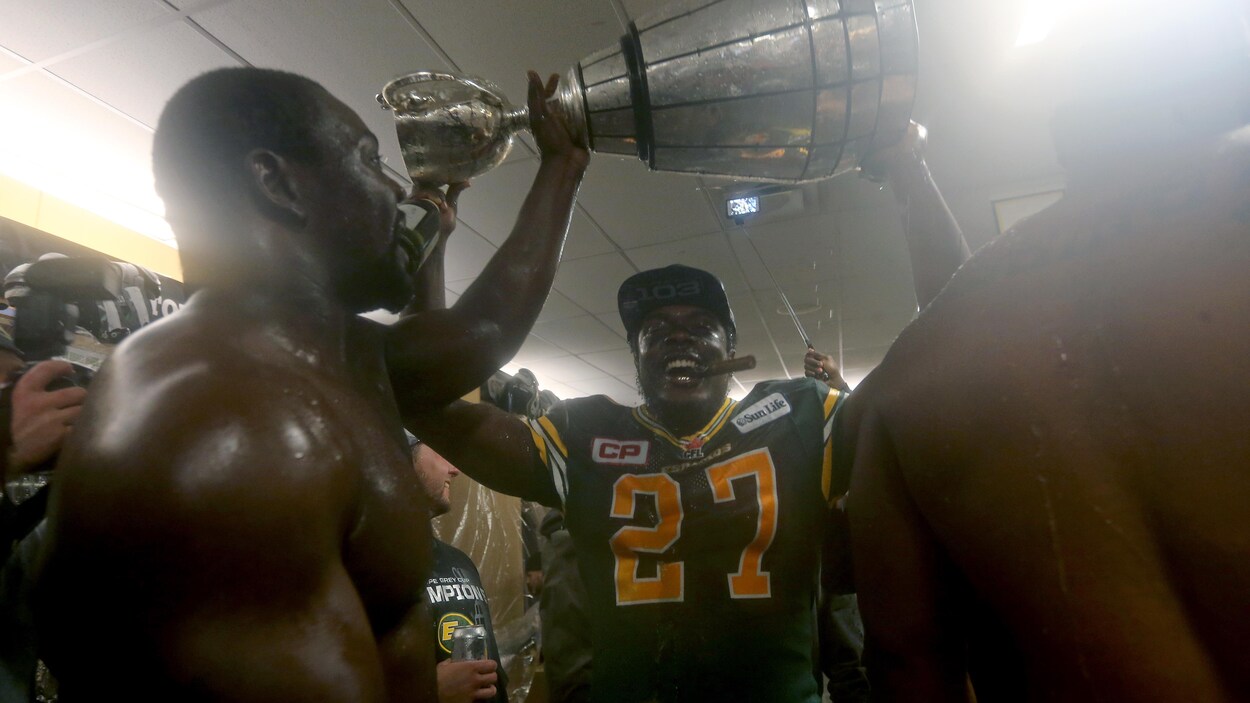 Un joueur des Eskimos, cigare à la bouche, soulève la Coupe Grey dans le vestiaire de l'équipe.
