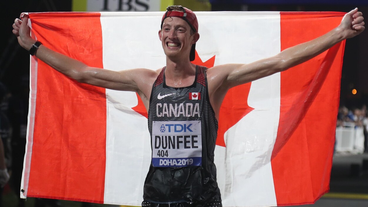 En sueur, il porte une casquette à l'envers et tient un drapeau du Canada derrière son dos.