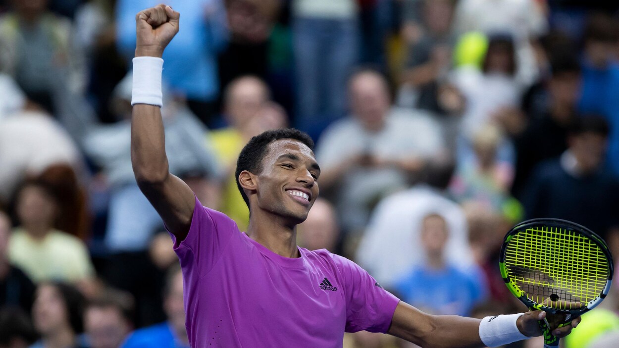 Un joueur de tennis, vêtu de mauve, lève les bras en souriant après une victoire importante. 