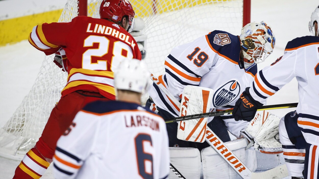 Le gardien des Oilers Mikko Koskinen cherche la rondelle, alors qu'Elias Lindholm la pousse derrière lui. Le gardien des Oilers Mikko Koskinen cherche la rondelle, alors qu'Elias Lindholm la pousse derrière lui.