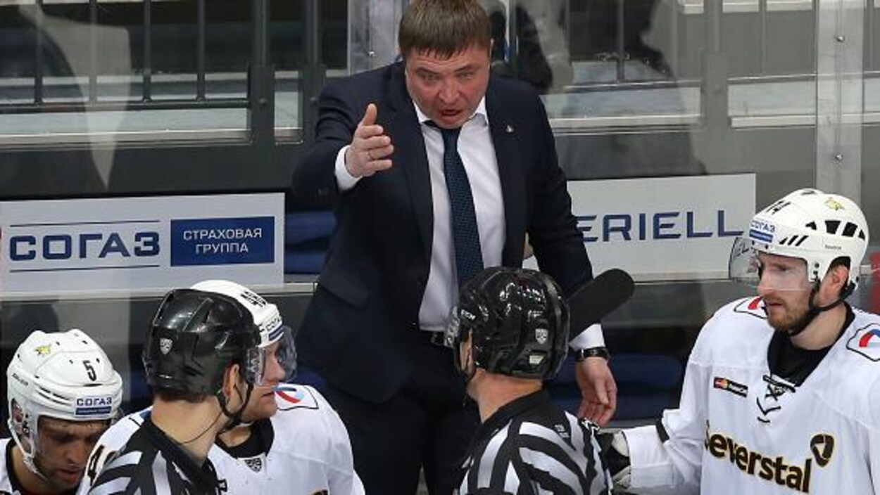 Un entraîneur parle à deux arbitres venus le voir à son banc.