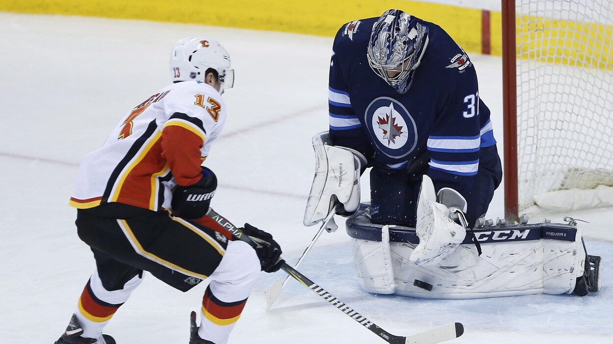 Le gardien des Jets de Winnipeg Connor Hellebuyck (à droite) réalise l'arrêt sur une échappée de Johnny Gaudreau, des Flames de Calgary.