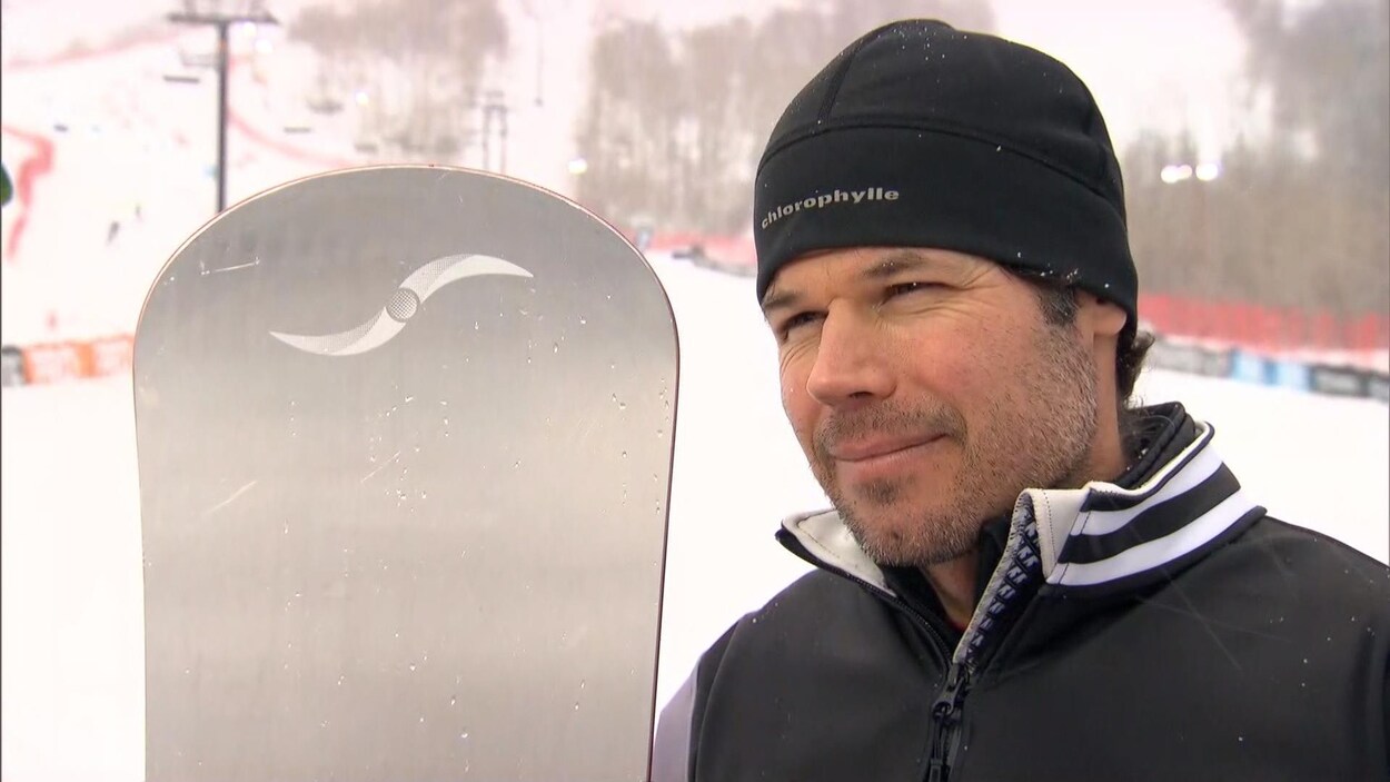 Il est debout devant une piste et tient sa planche.