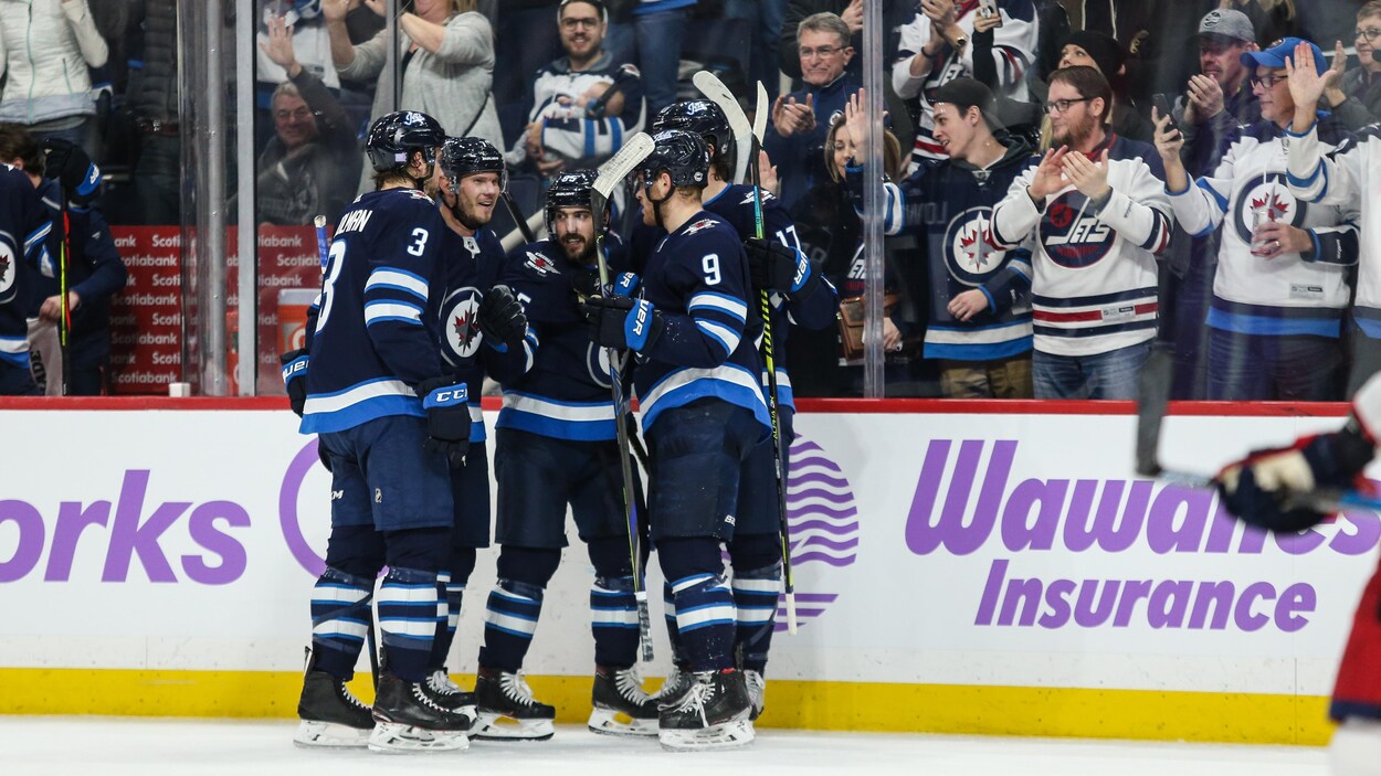 Des supporteurs applaudissent cinq joueurs des Jets de Winnipeg réunis devant la baie vitrée.