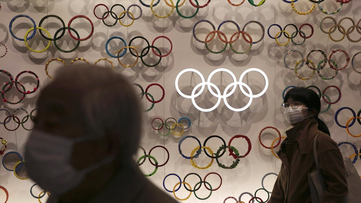 Des visiteurs qui portent des masques se promènent parmi les anneaux olympiques dans le musée olympique de Tokyo.