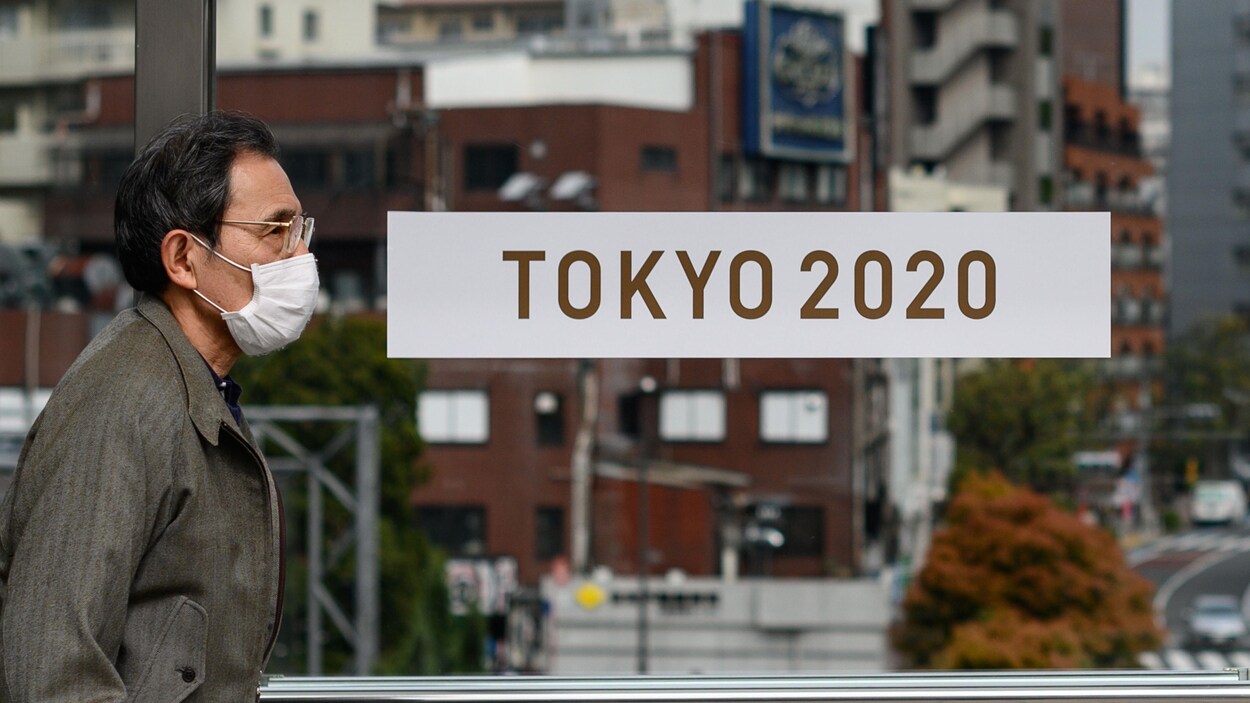 Un passant avec un masque marche devant une affiche des Jeux olympiques à Tokyo.