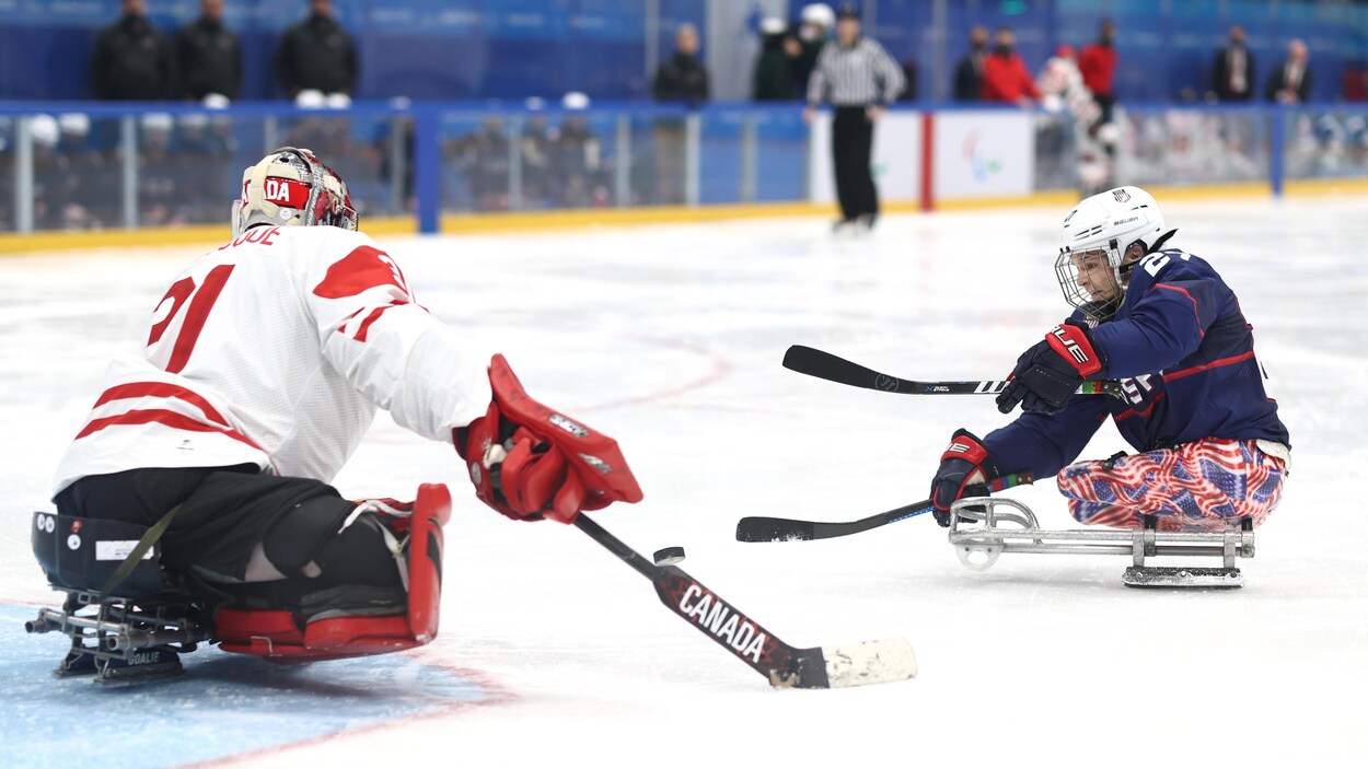 Un gardien de parahockey canadien se dresse devant un attaquant américain en tir de pénalité.