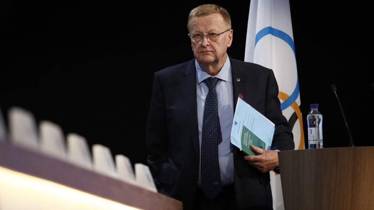 John Coates quitte le podium avec des documents à la main gauche.