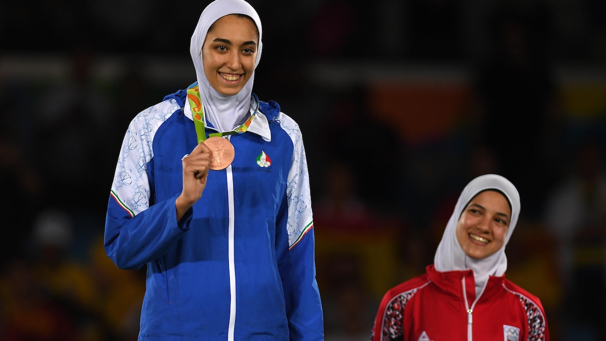 Elle montre sa médaille sur le podium.
