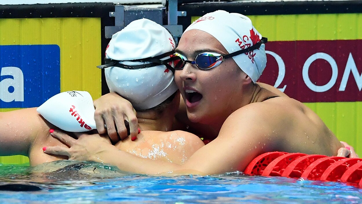 Deux nageuses se félicitent dans la piscine, près du mur, après leur course.