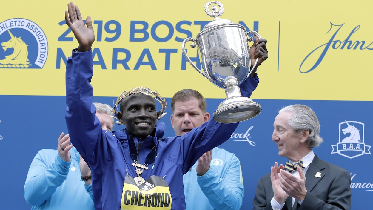Il tient le trophée dans la main gauche.