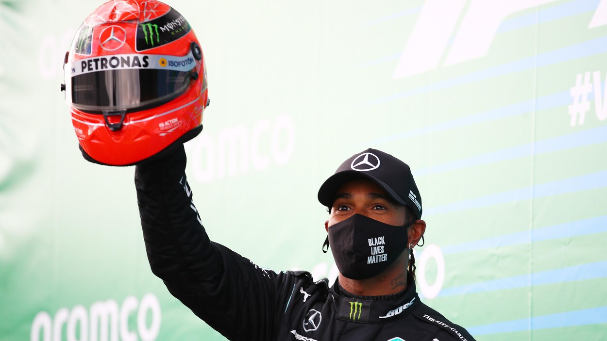 Lewis Hamilton lève un casque rouge de sa main gauche.