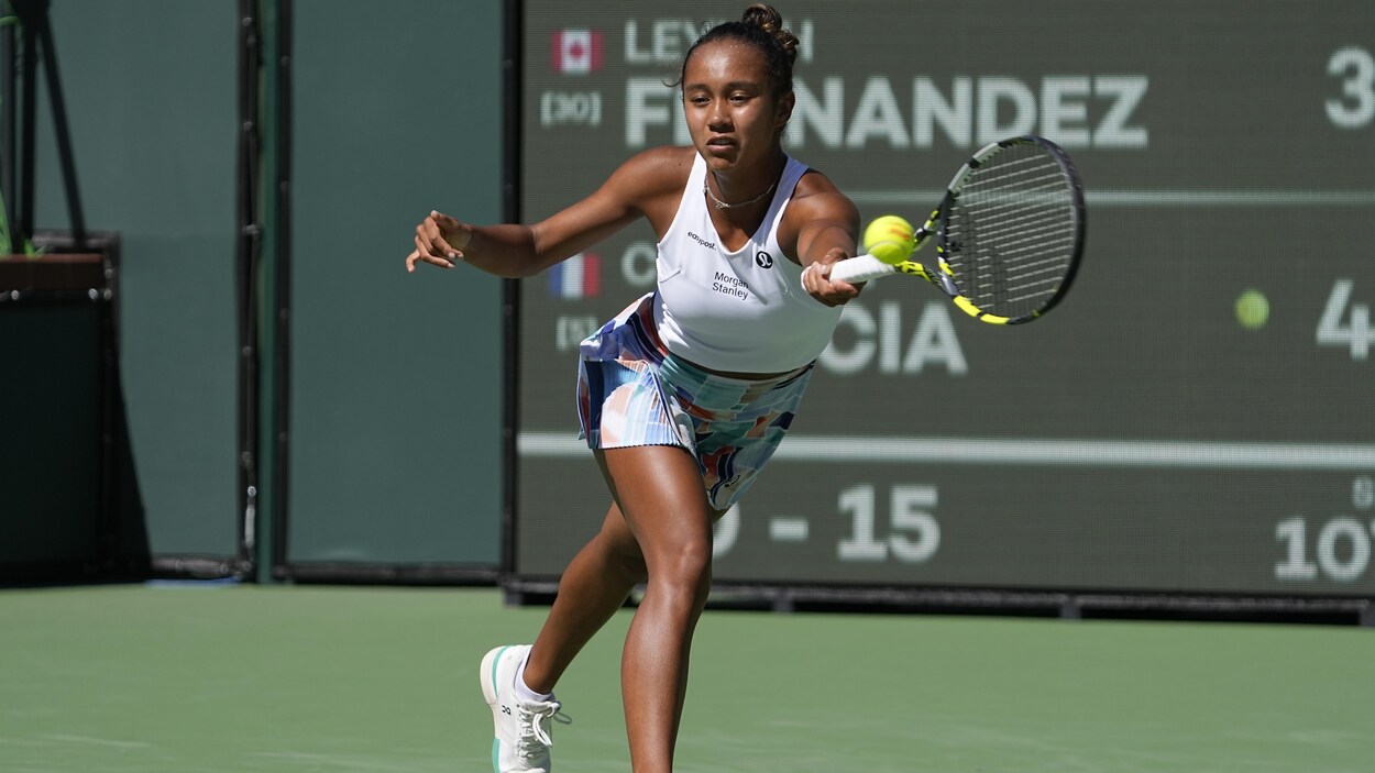Arborant un haut sportif blanc et une jupe multicolore, Leylah Annie Fernandez étire la raquette pour retourner difficilement la balle à son adversaire Caroline Garcia.