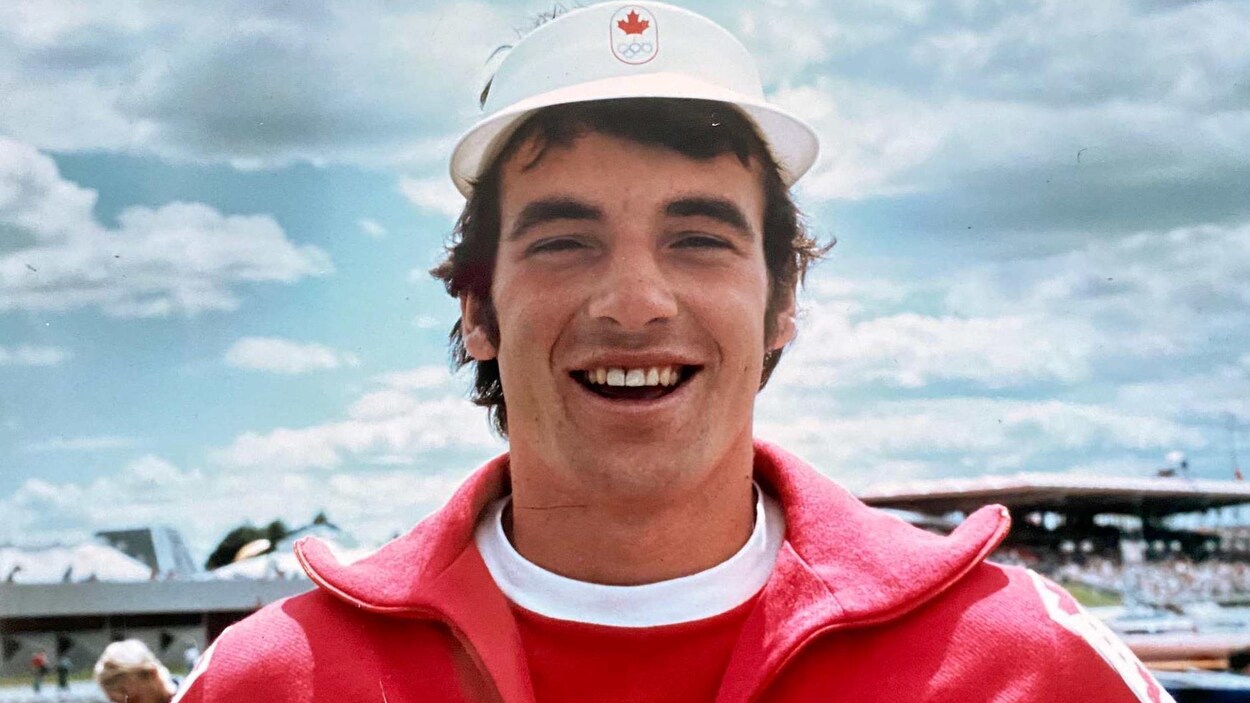Il sourit et arbore une veste et chapeau aux couleurs de l'équipe canadienne.