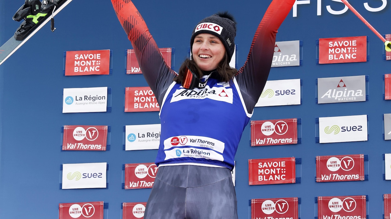 Elle tient un ski dans sa main droite et un bâton dans celle de gauche sur le podium.