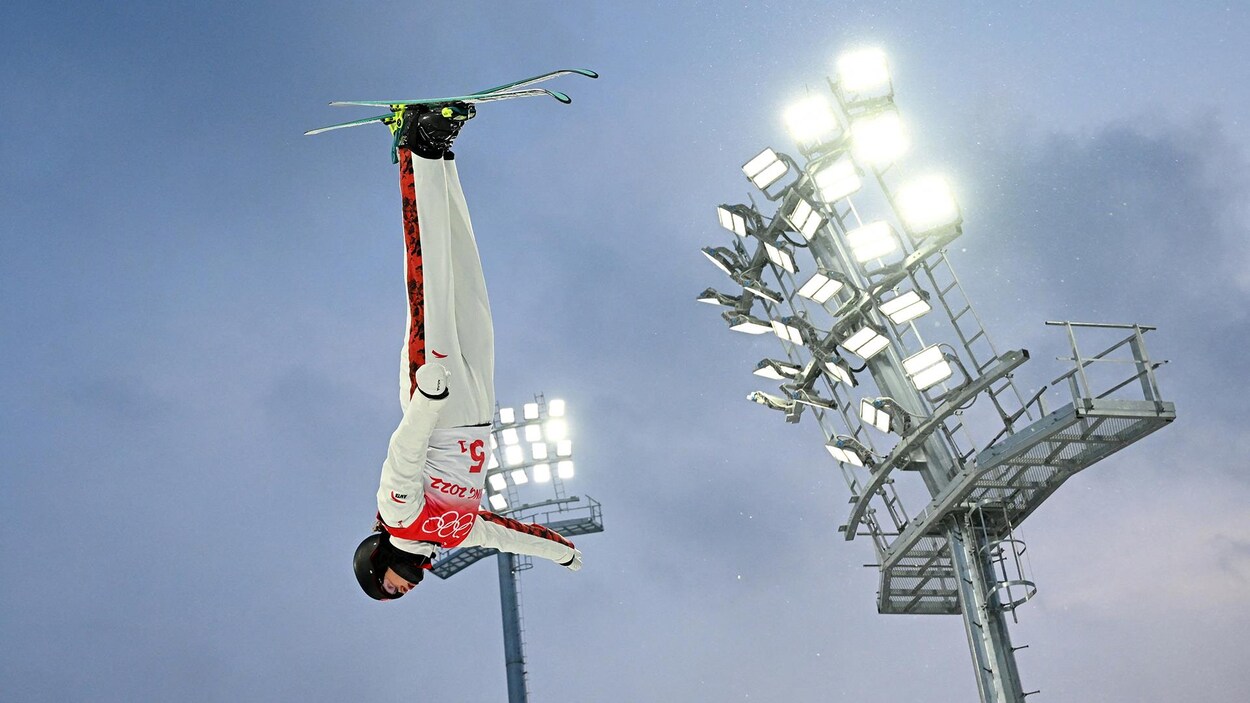 Une skieuse acrobatique a la tête en bas pendant un saut.