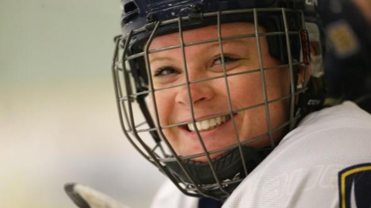 Une joueuse de hockey souriante porte un casque muni d'une grille.