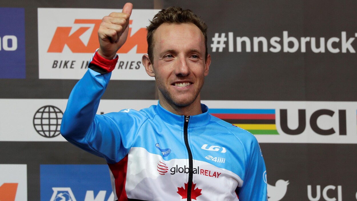 Avec son chandail de l'équipe nationale du Canada, il lève le pouce en souriant.
