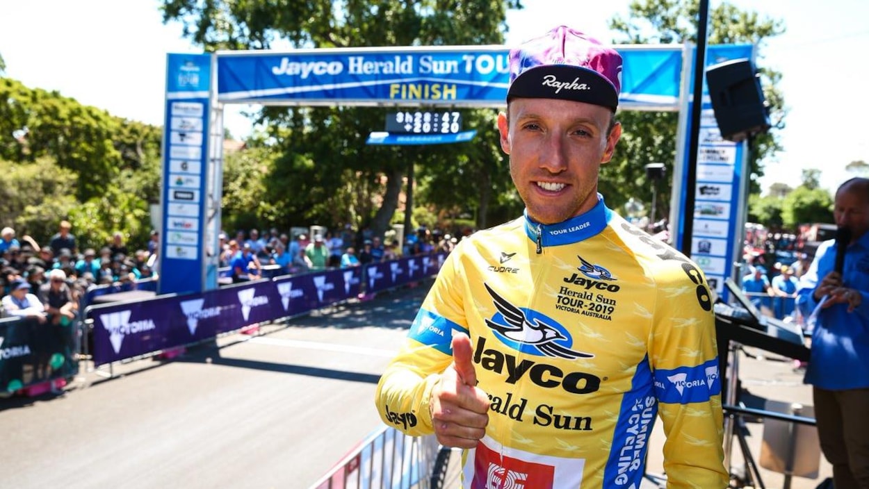 Woods vêtu de son maillot jaune sourit à la caméra en levant le pouce près de la ligne d'arrivée.